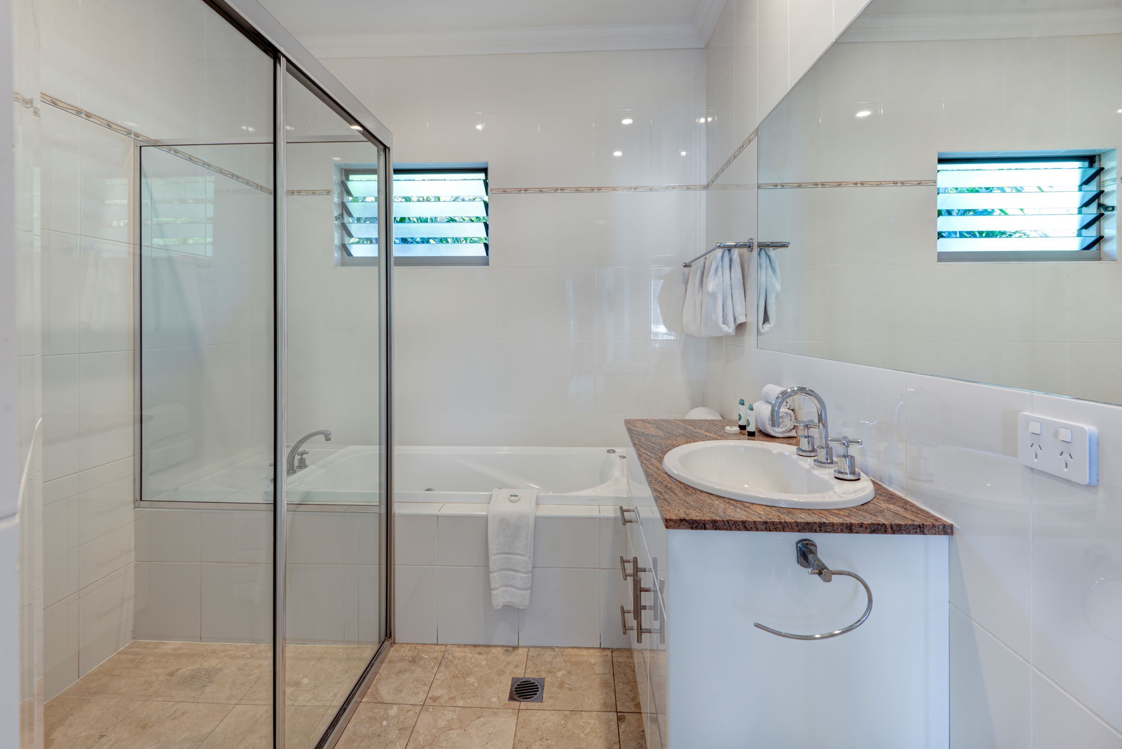 Un baño moderno con ducha de vidrio, bañera, lavamanos con encimera de mármol y un espejo grande.