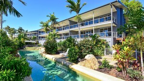 A hotel with a swimming pool, surrounded by tropical plants and palm trees.