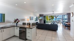 A modern kitchen with a built-in dishwasher, a dining area with a table and chairs, and a living room with a sofa and a view of the ocean.