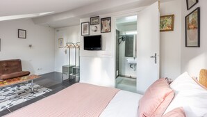A modern bedroom with a bed, a bench, a TV, and a bathroom visible through an open door. - Vincennes Sauvage  (Vincennes)