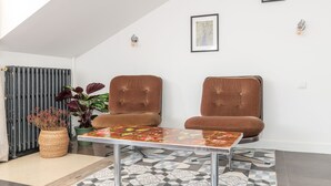 A modern living room with two brown woven chairs, a glass coffee table, a patterned rug, and a radiator. - Vincennes Sauvage  (Vincennes)