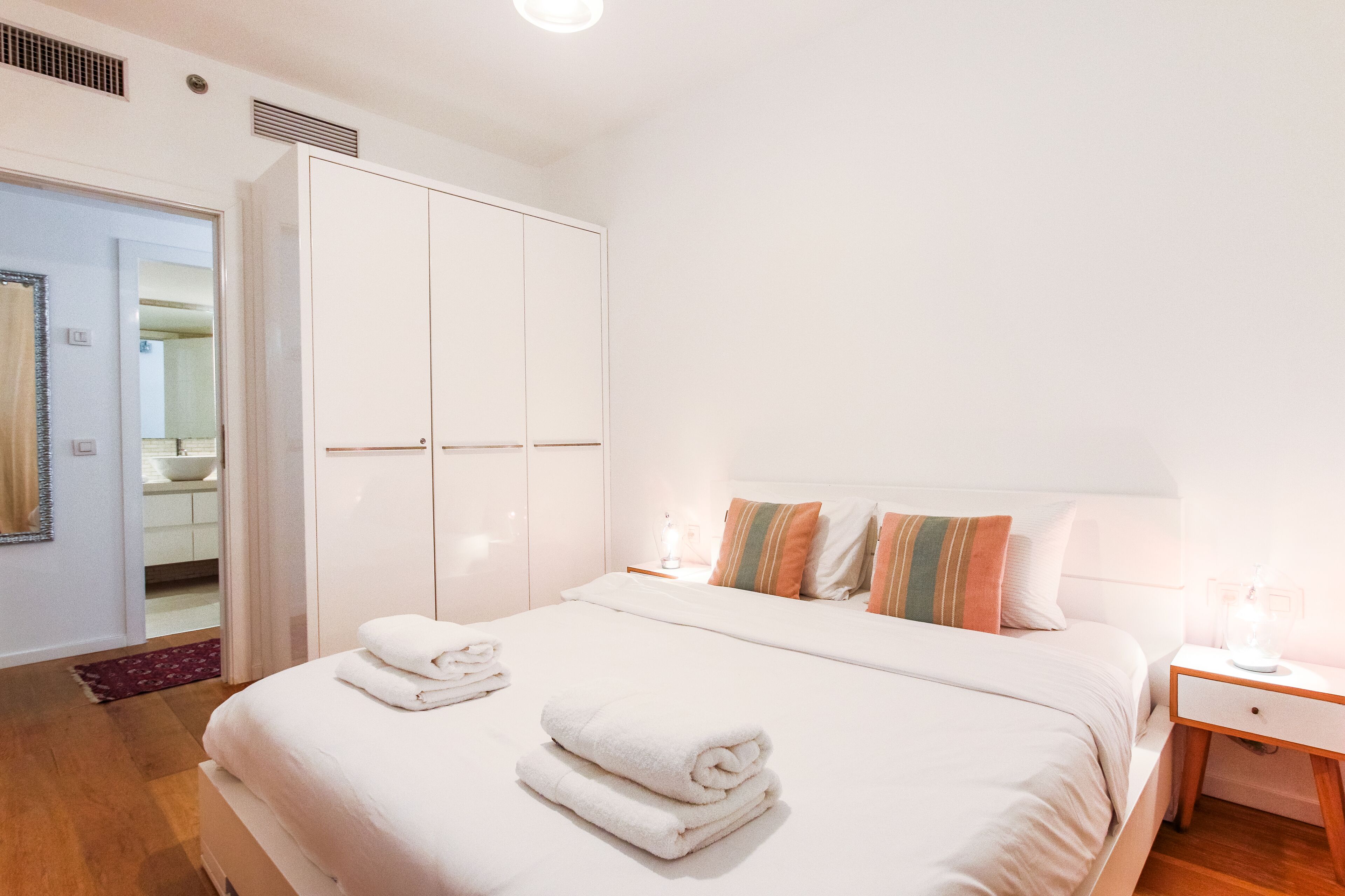 A hotel room with a large bed, a wardrobe, a bedside table with a lamp, and a bathroom visible through an open door.