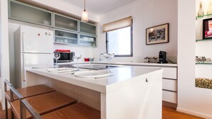 A modern kitchen with a central island, white cabinetry, and a window with a view. - Luxury Condo & Spectacular View by FeelHome (Tel Aviv)