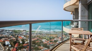 A balcony with a wooden table and chairs, overlooking a coastal town with red-roofed buildings and a clear view of the ocean. - Luxury Condo & Spectacular View by FeelHome (Tel Aviv)