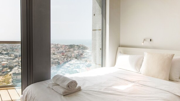 A modern hotel room with a large window offering a city view, a neatly made bed, and a clean, minimalist design. - Luxury Condo & Spectacular View by FeelHome (Tel Aviv)