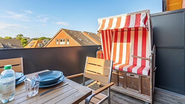 Ein Balkon mit Tisch, Stühlen und einem gestreiften Sonnenschirm.