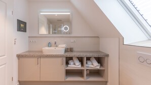 Ein modernes Badezimmer mit Oberlicht, großem Spiegel, Waschbecken und ordentlich gefalteten Handtüchern auf Regalen.