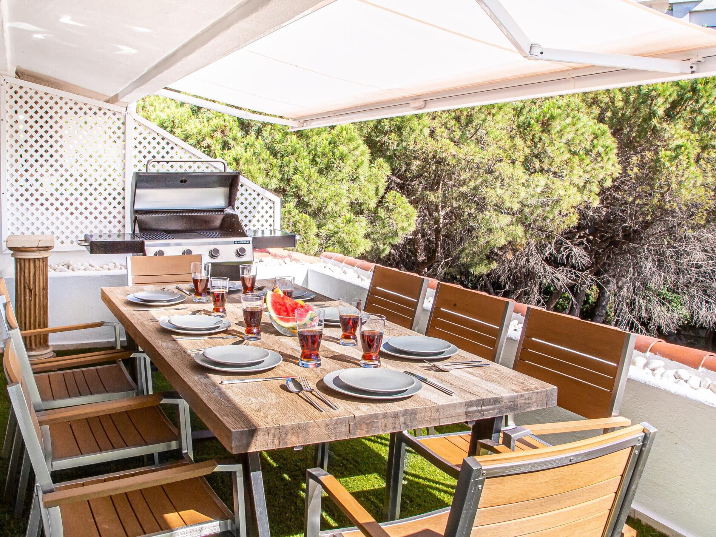 An outdoor dining area with a wooden table, chairs, and a grill.