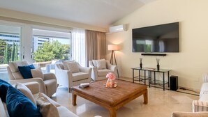 A modern living room with a large flat-screen TV, comfortable seating, and a view of greenery outside. - Luxurious penthouse in Marbella with pool, WiFi, pets allowed, air conditioning (Marbella)