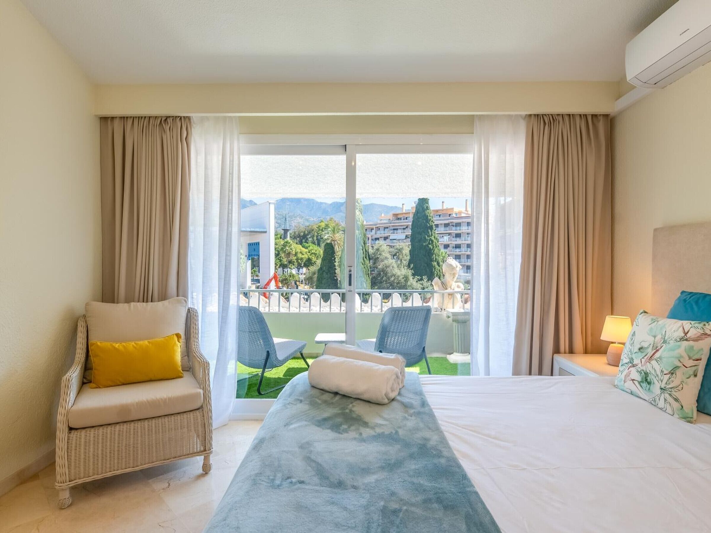 Habitación de hotel con una cama, una silla, una mesita y vistas a la ciudad.