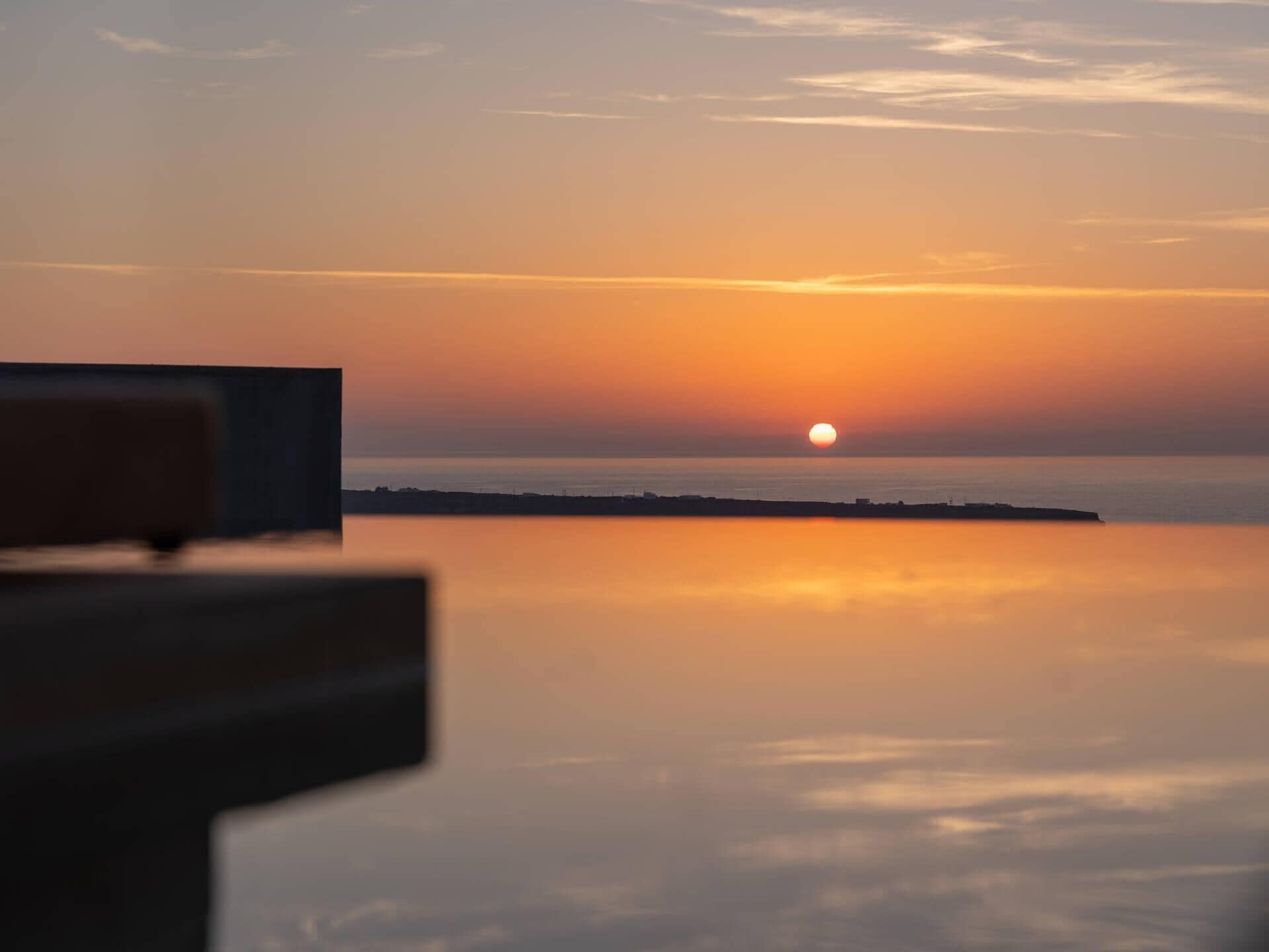 A sunset over a calm sea with a distant shoreline.