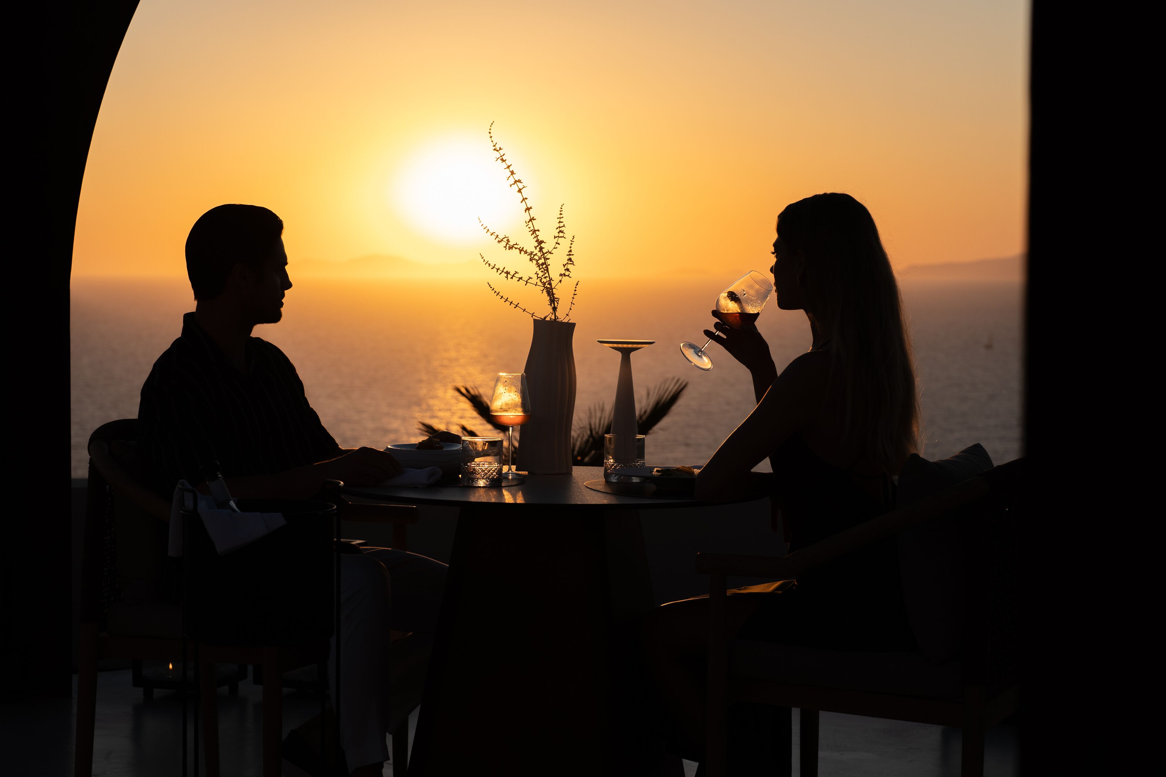 Un couple est assis à une table d’où l’on peut admirer le coucher de soleil sur l’océan.