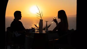 A couple at a table with a view of the sunset over the ocean.