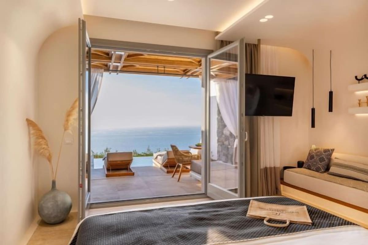 A bedroom with a bed, a TV, a sofa, and a view of the sea.