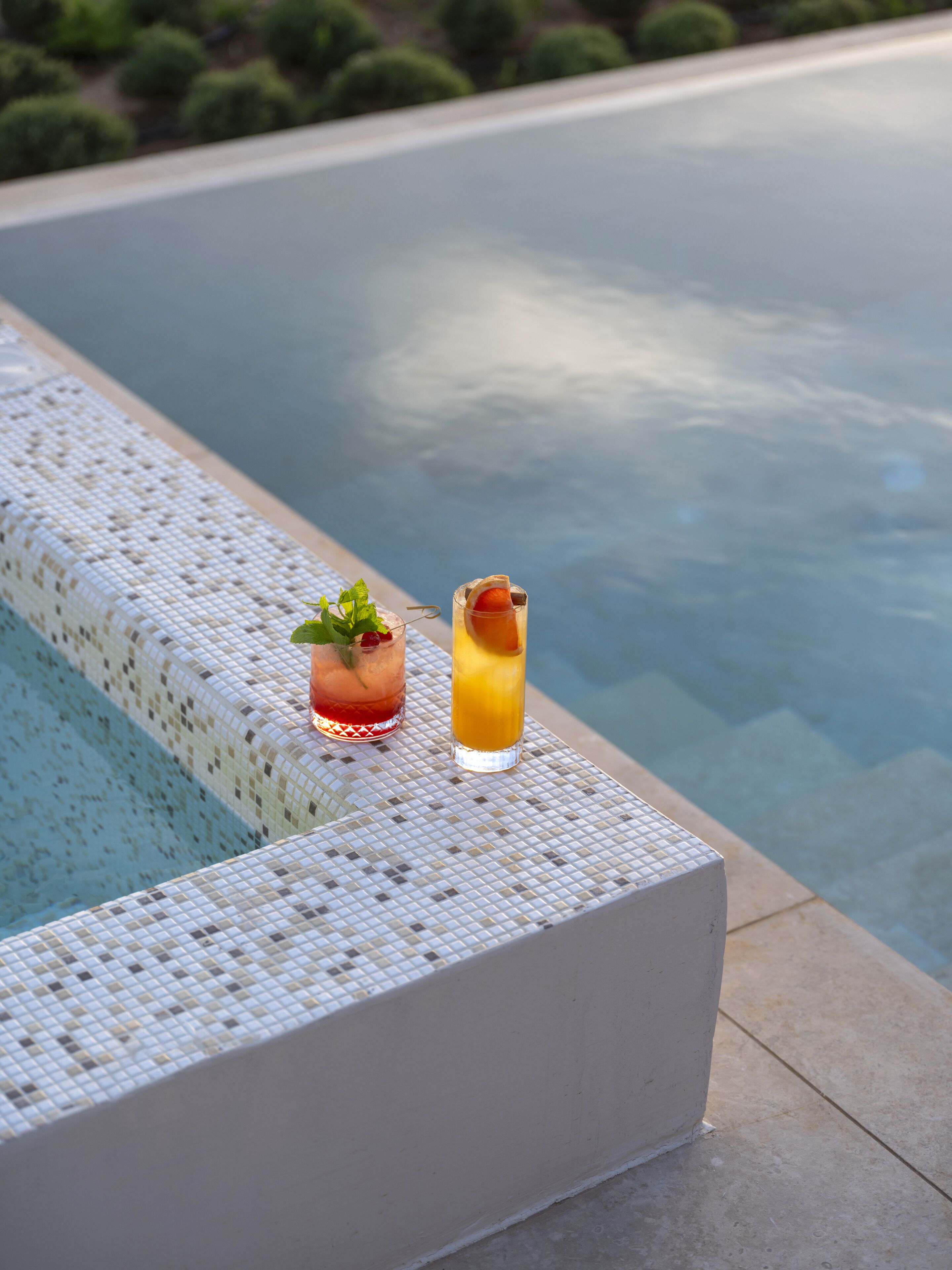 Deux cocktails sur une petite table en osier blanc, près d’une piscine.