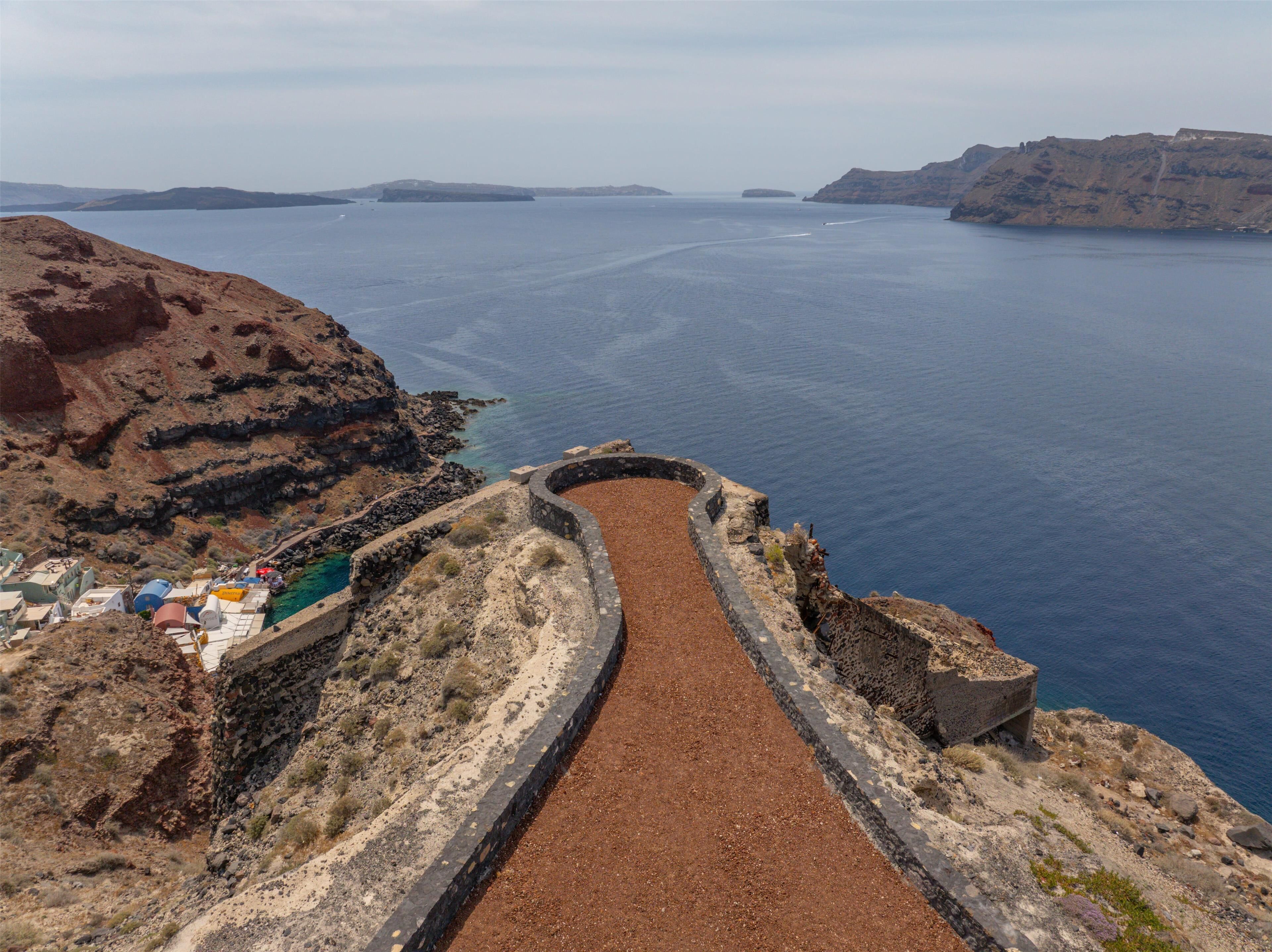 A coastal path leading to a cliff edge with a view of the sea and distant islands.