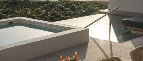 A poolside area with a table of fruit, a lounge chair, and a view of the sea.