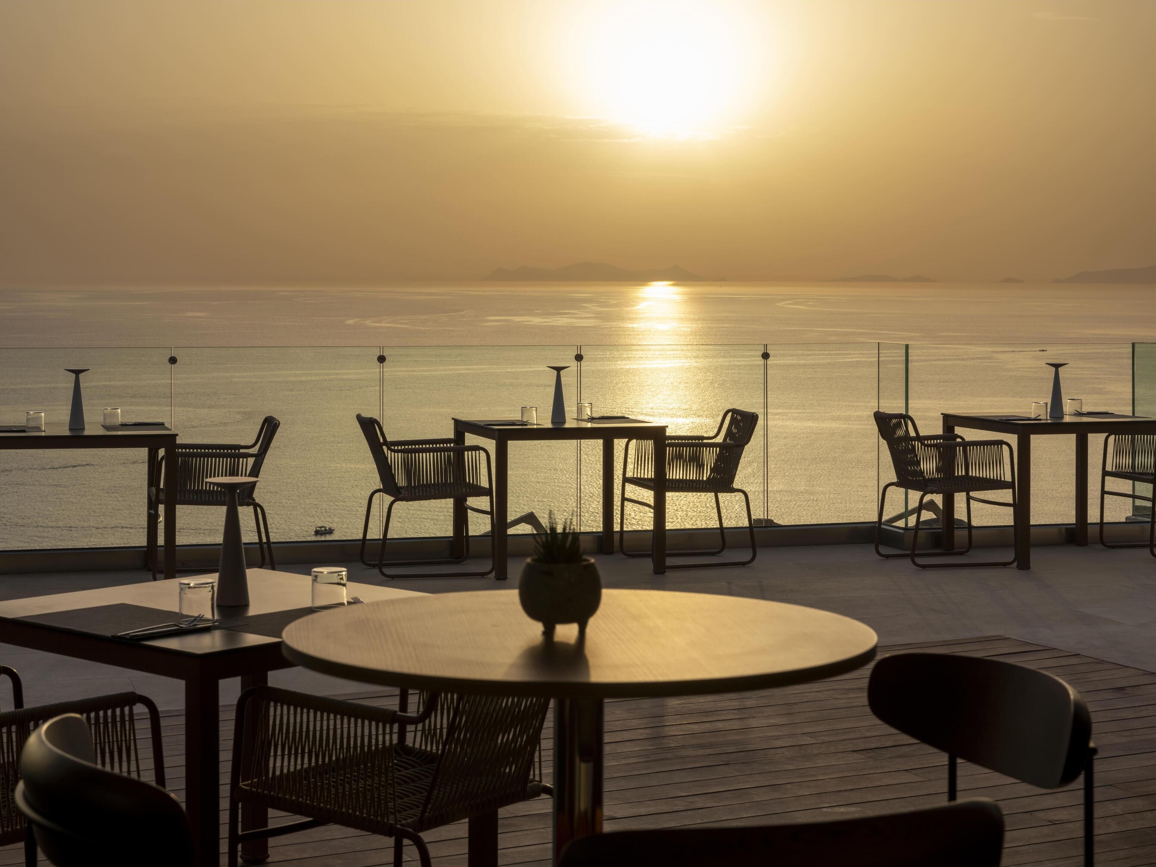 Terraza con mesas y sillas que da a un mar tranquilo al atardecer.