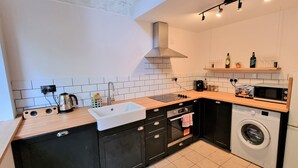 A compact kitchen with a sink, stove, microwave, and washing machine. - Seafront Apartment with Garden - Perfect location in Mumbles (Swansea)