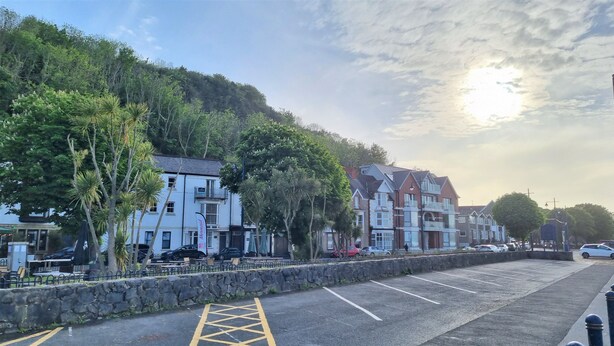 A row of residential buildings with a stone wall and trees in the foreground. - Seafront Apartment with Garden - Perfect location in Mumbles (Swansea)