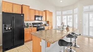 A modern kitchen with wooden cabinets, a black refrigerator, a stainless steel microwave, a gas stove, and a granite countertop.