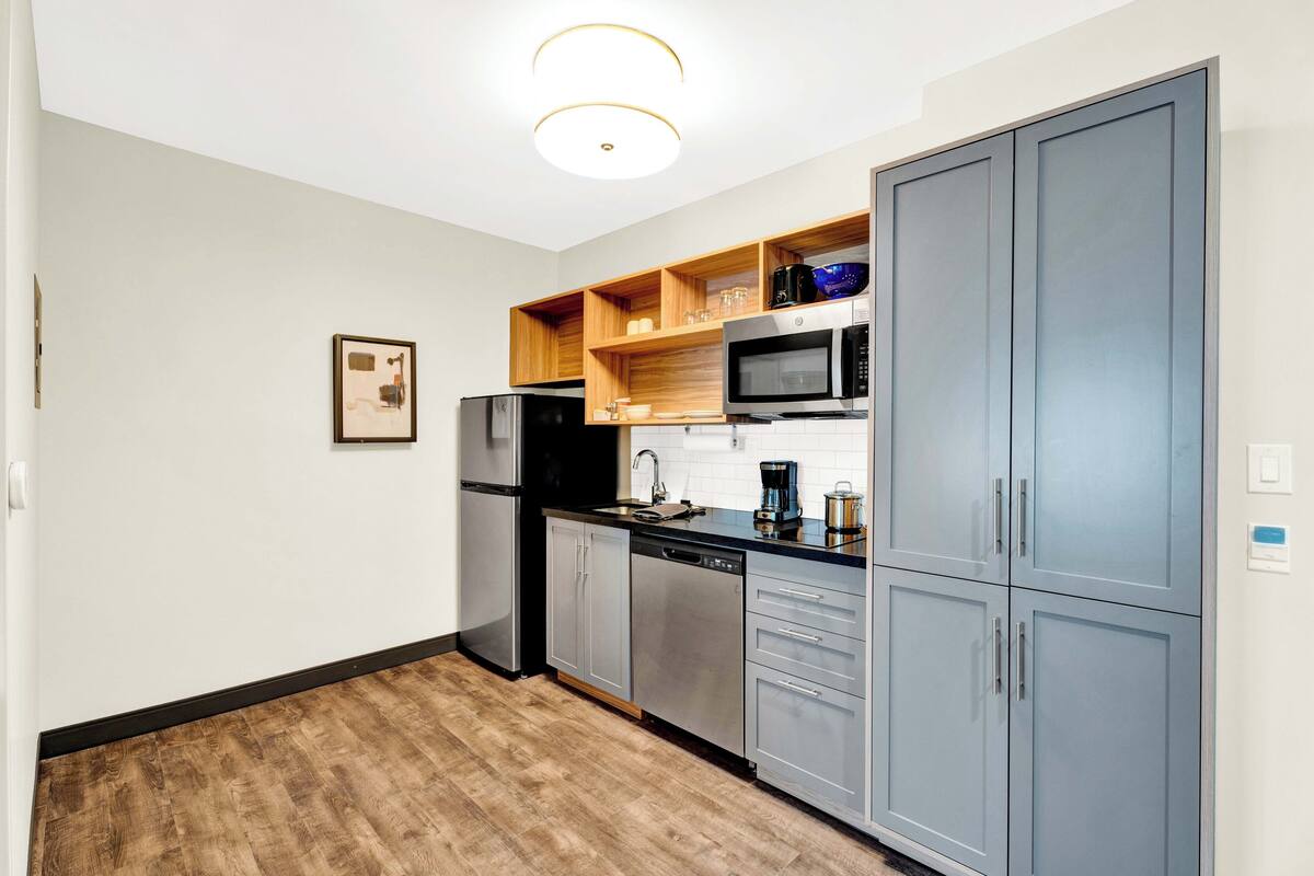 A modern kitchen with stainless steel appliances, wooden shelves, and grey cabinets.