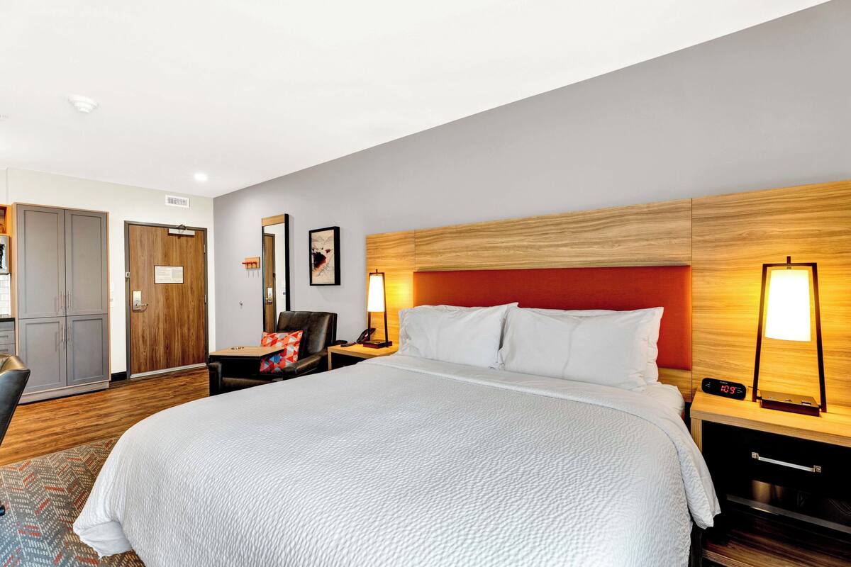 A hotel room with a large bed, wooden headboard, bedside lamps, a desk, and a wardrobe.