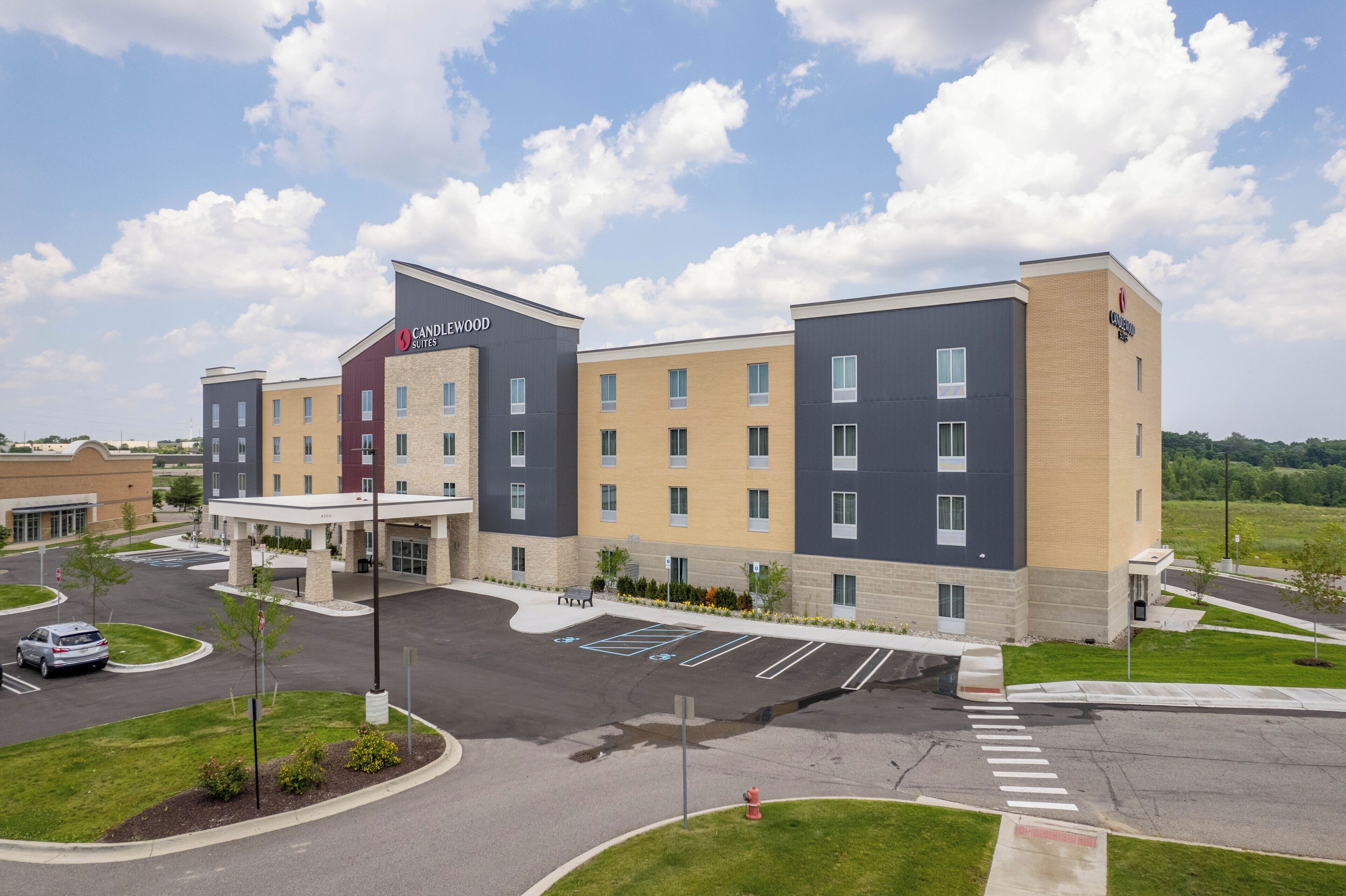 A multi-story hotel with a modern design, featuring a mix of brick and glass facades, a central courtyard, and a parking lot with marked spaces.