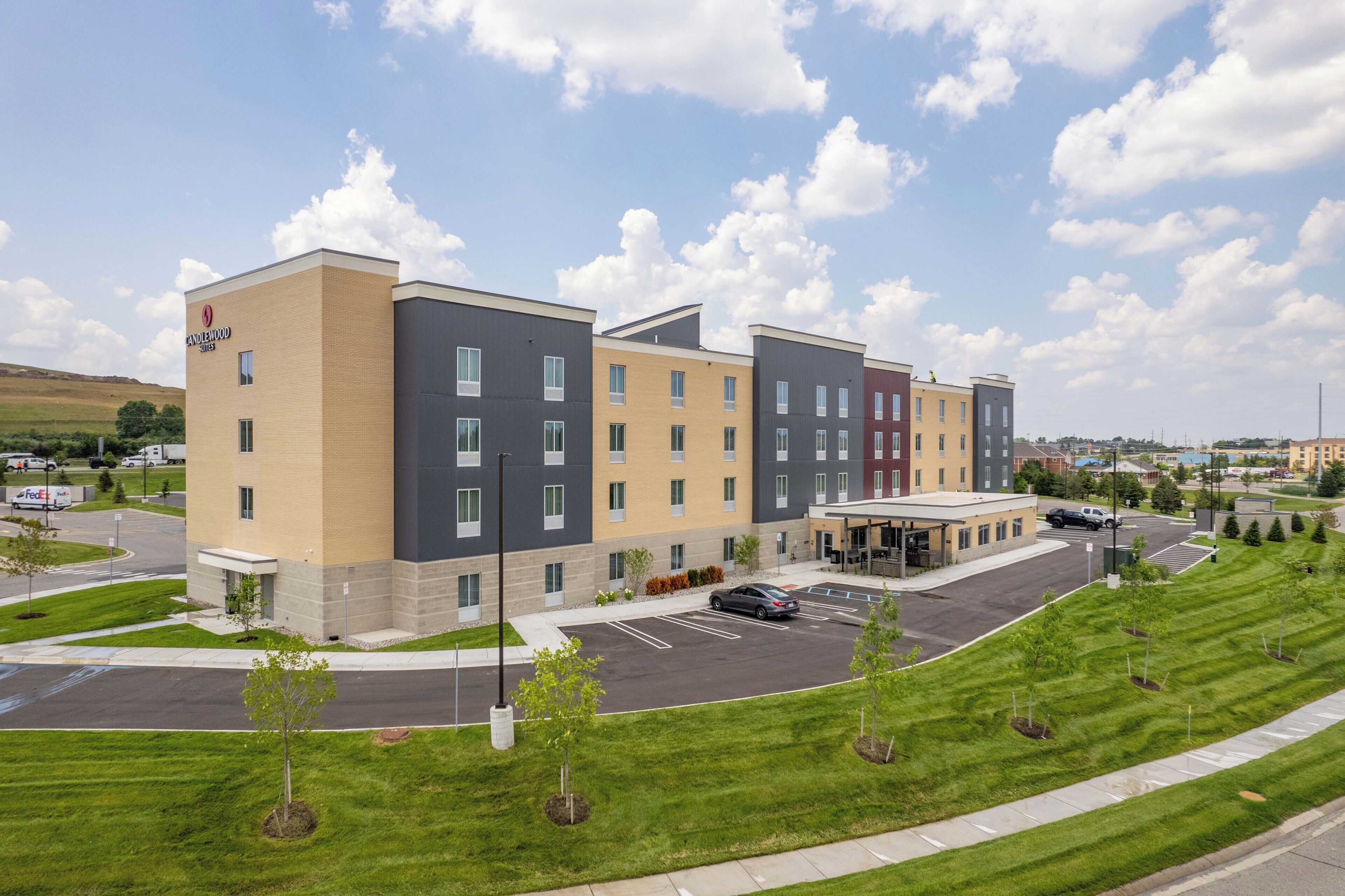 A multi-story hotel with a parking lot and a landscaped area with young trees.