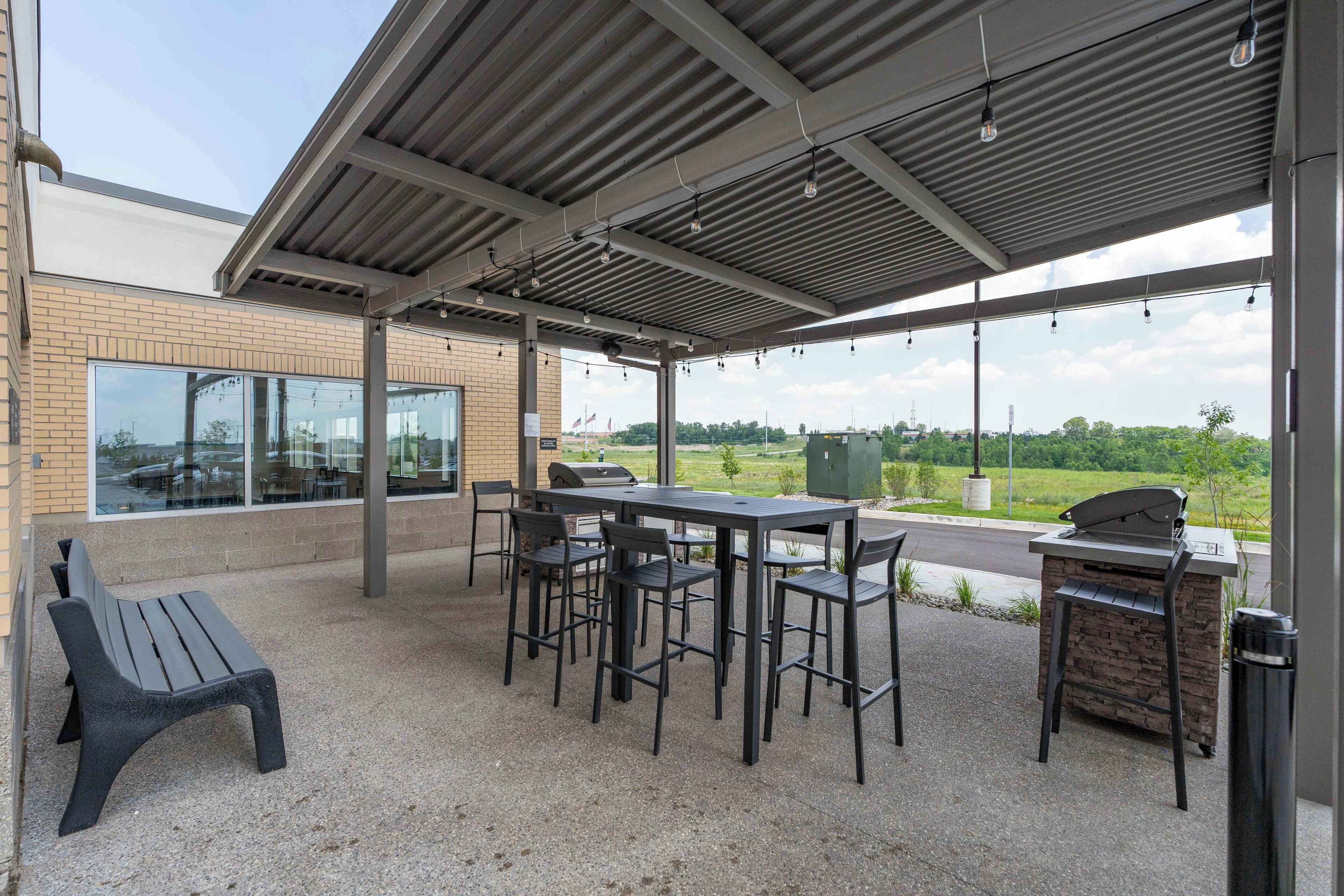 An outdoor patio with a table and chairs, a grill, and a trash can.