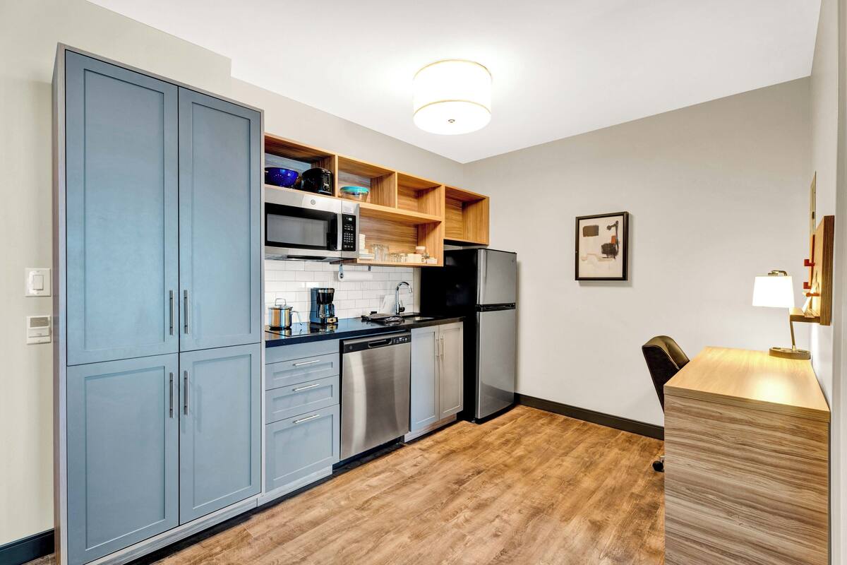 A modern kitchen with grey cabinets, stainless steel appliances, and wooden shelves.