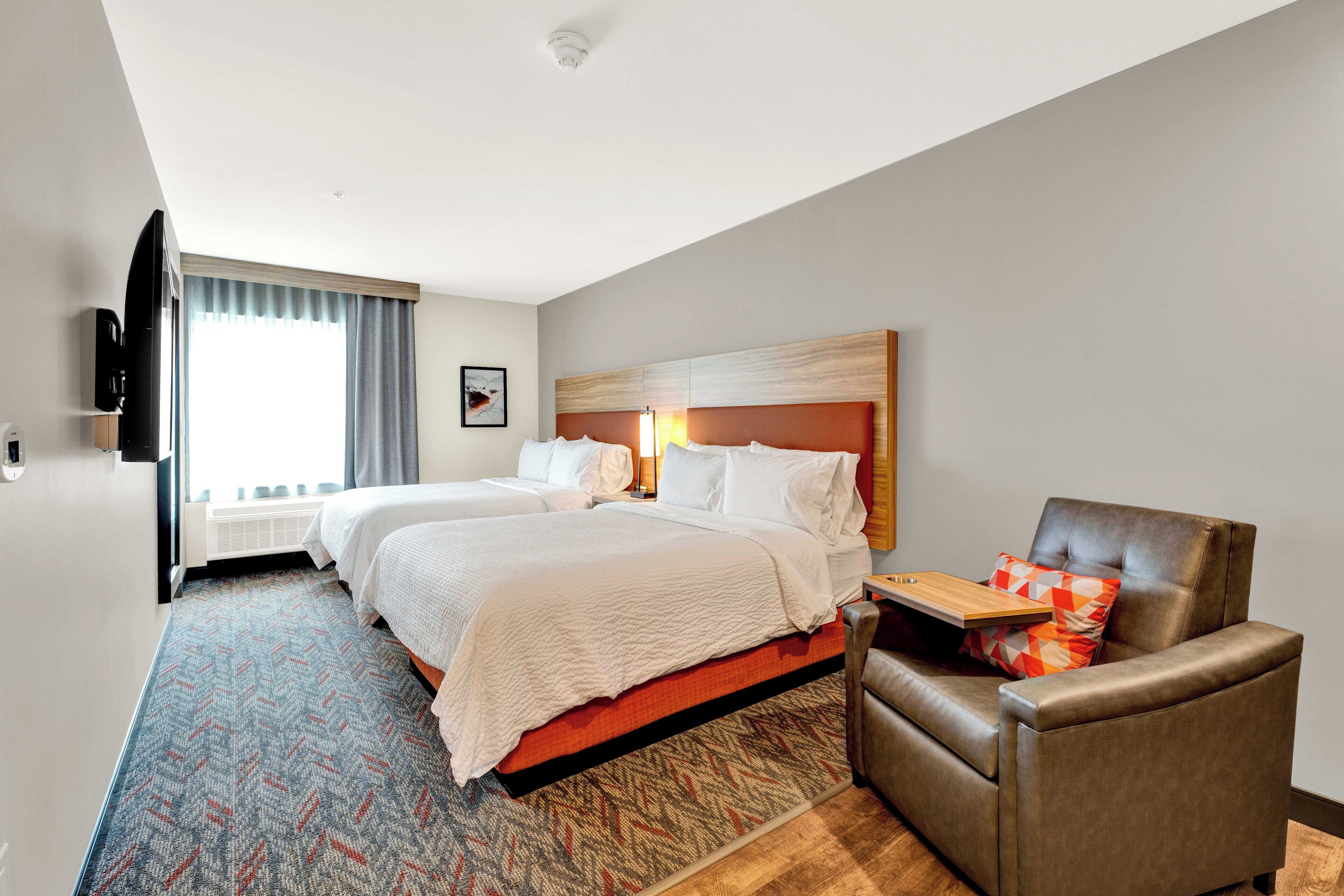 Habitación de hotel con dos camas, un sofá, un televisor de pantalla plana y una ventana con cortinas.