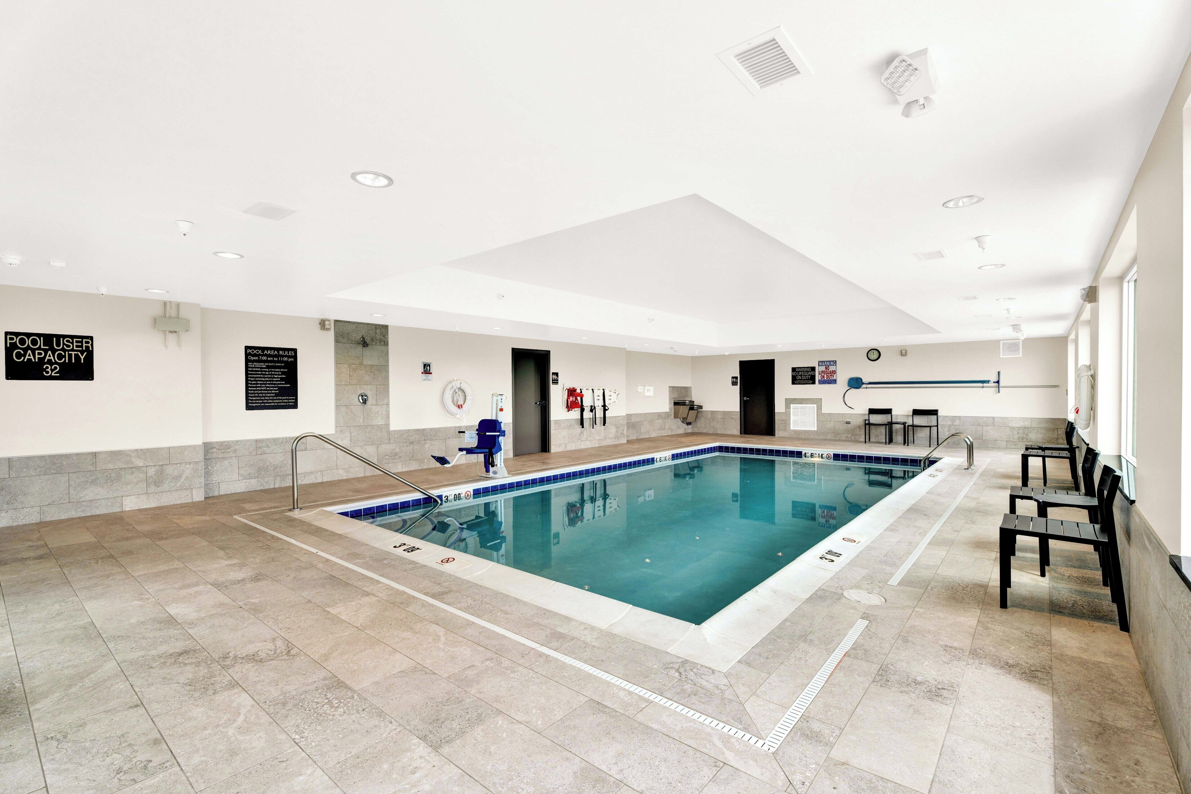A large indoor swimming pool with a capacity sign, safety equipment, and seating along the walls.