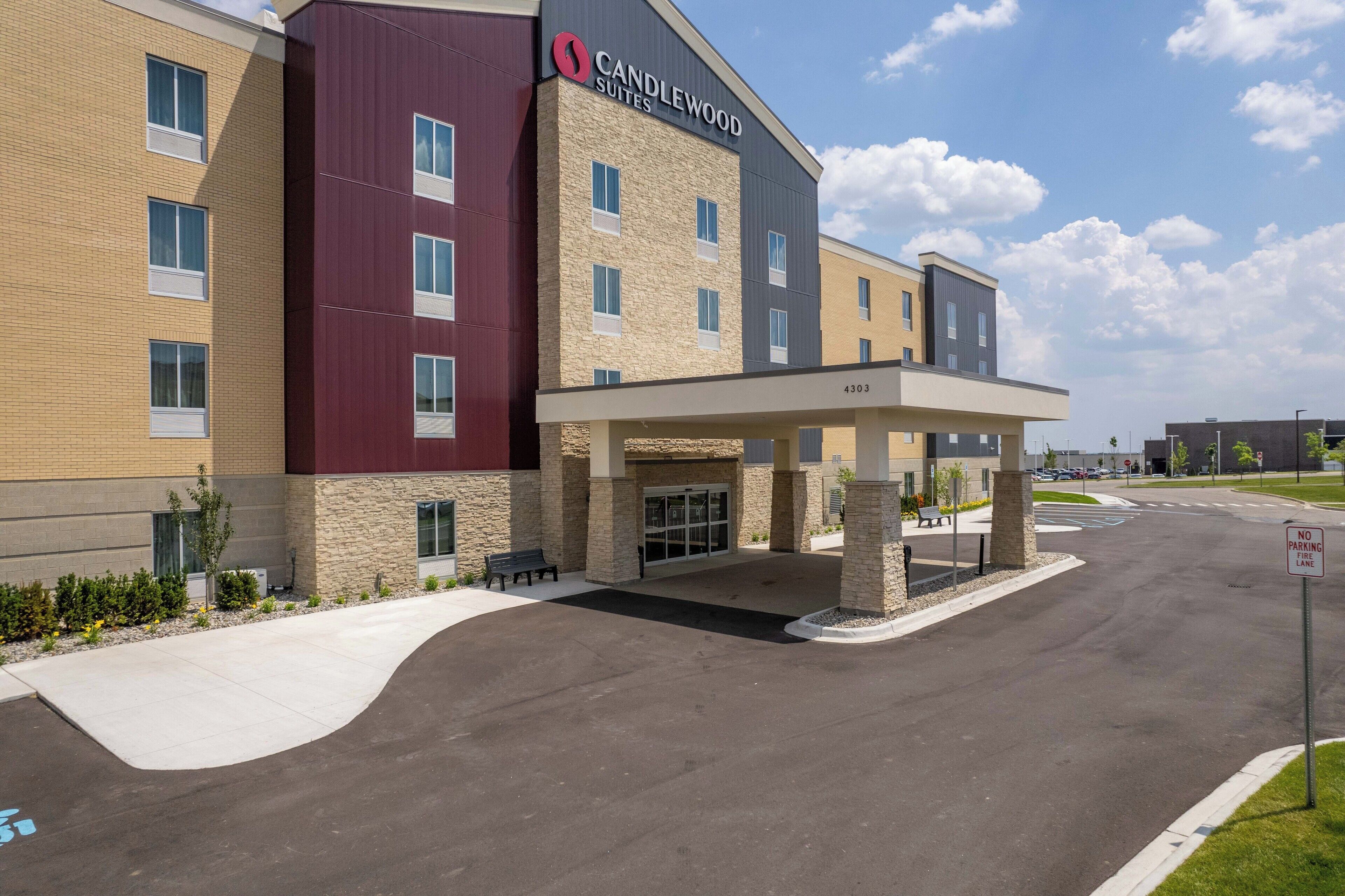 A multi-story hotel with a maroon and beige facade, a covered entrance, and a clear sky.