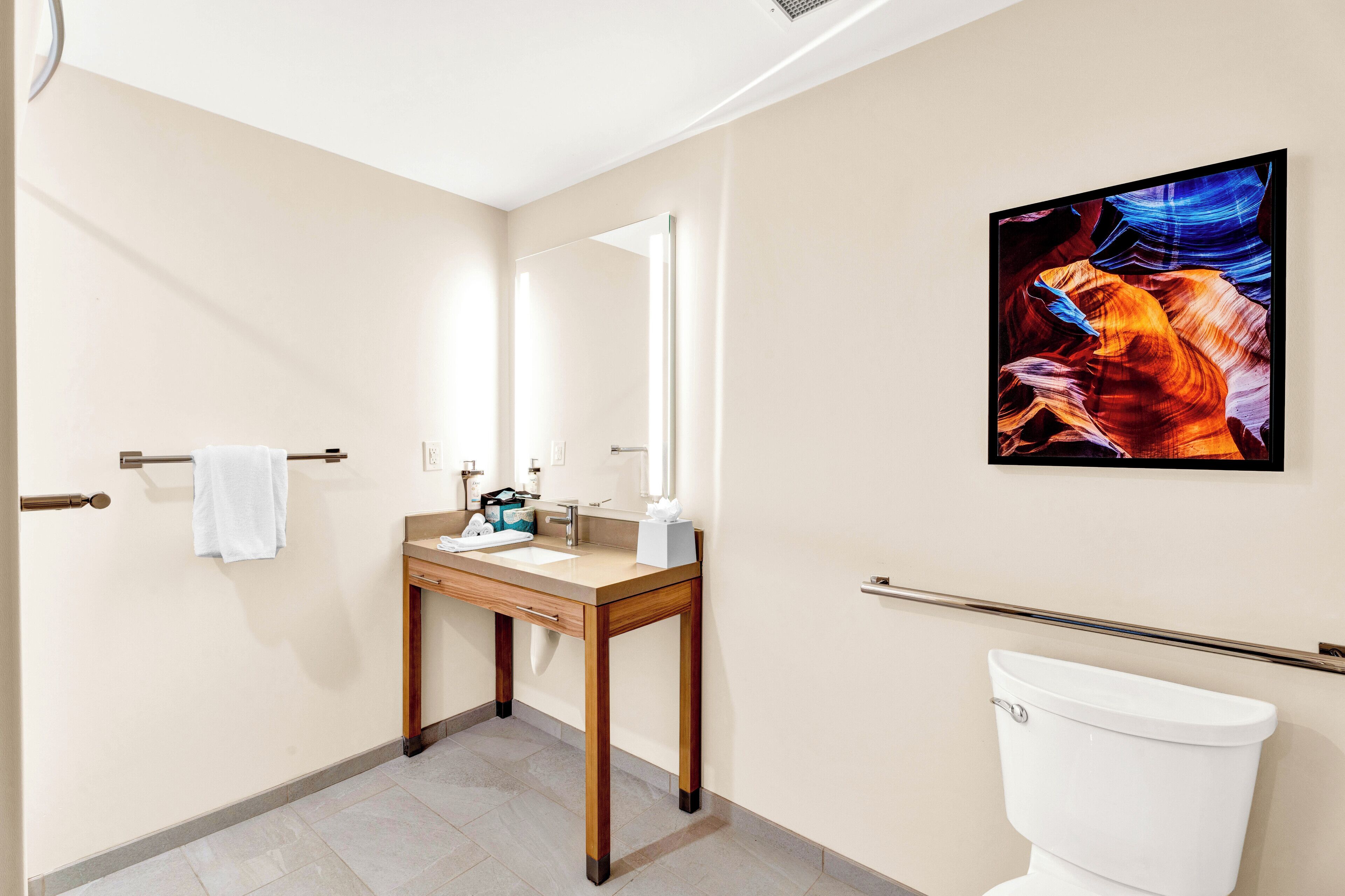A modern bathroom with a wooden vanity, a large mirror, and a framed artwork on the wall.