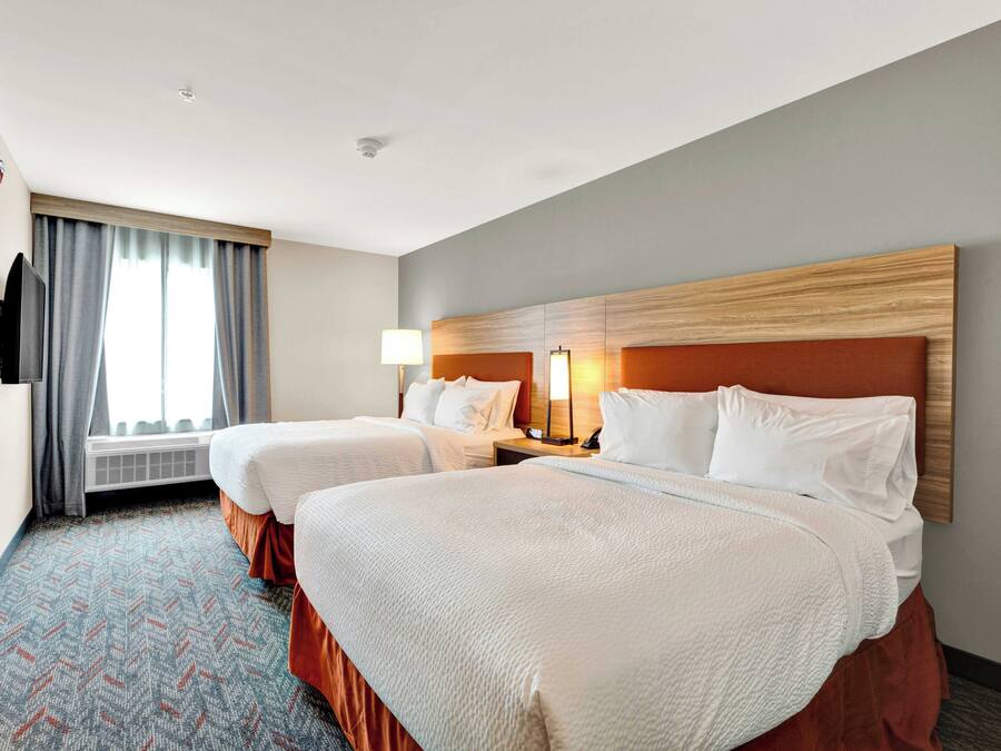 A hotel room with two beds, a TV, a desk with a lamp, and a window with curtains.