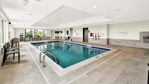 An indoor swimming pool with clear water, a diving board, and a seating area with chairs. - Candlewood Suites Detroit - Auburn Hills by IHG (Auburn Hills)