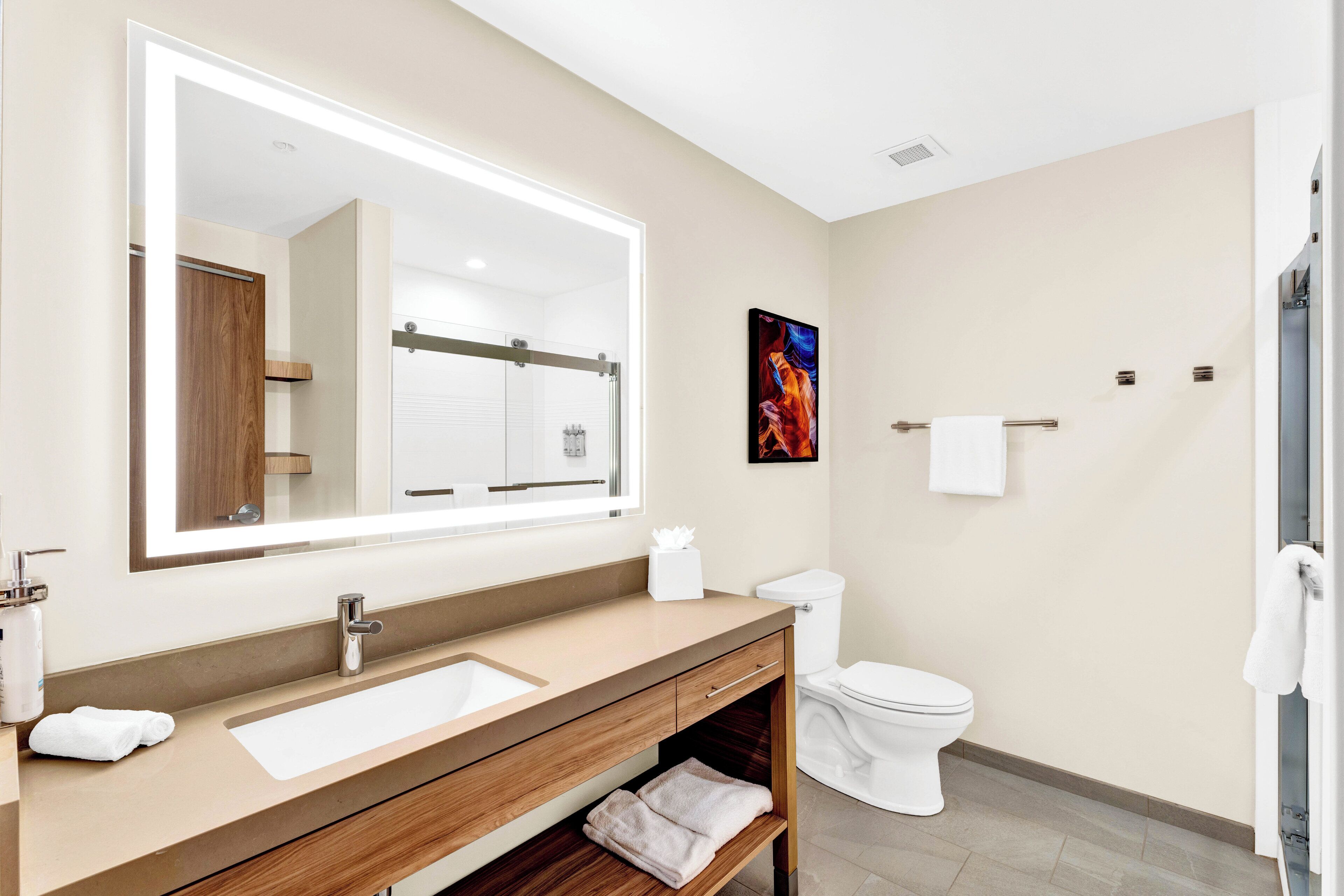 A modern bathroom with a large mirror, a sink, a toilet, and a shower area.