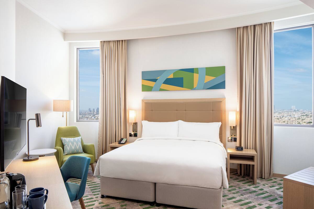 Een hotelkamer met een groot bed, een bureau, een stoel, een televisie en uitzicht over de stad.