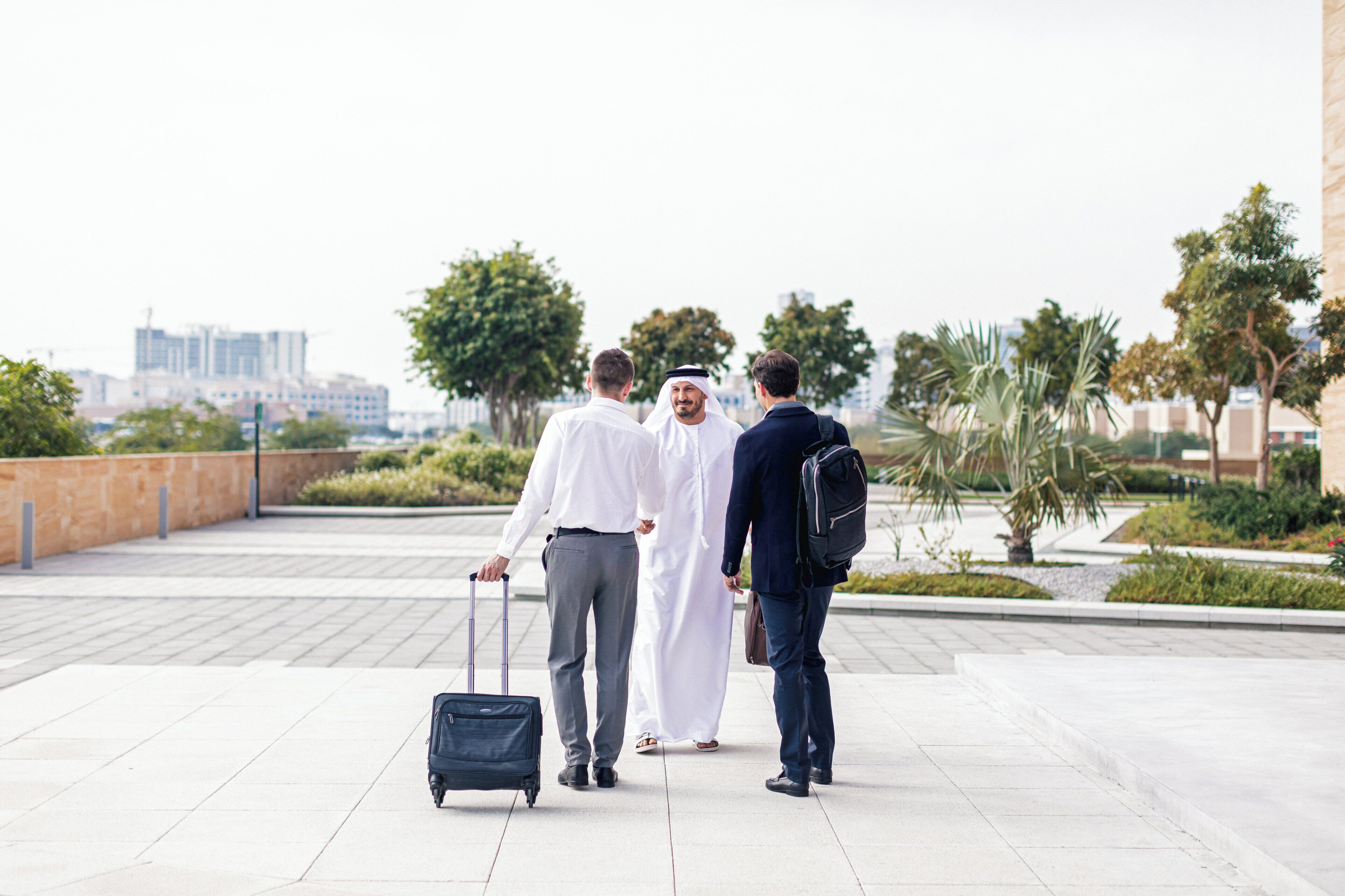 Three individuals walking on a paved pathway with a cityscape in the background.