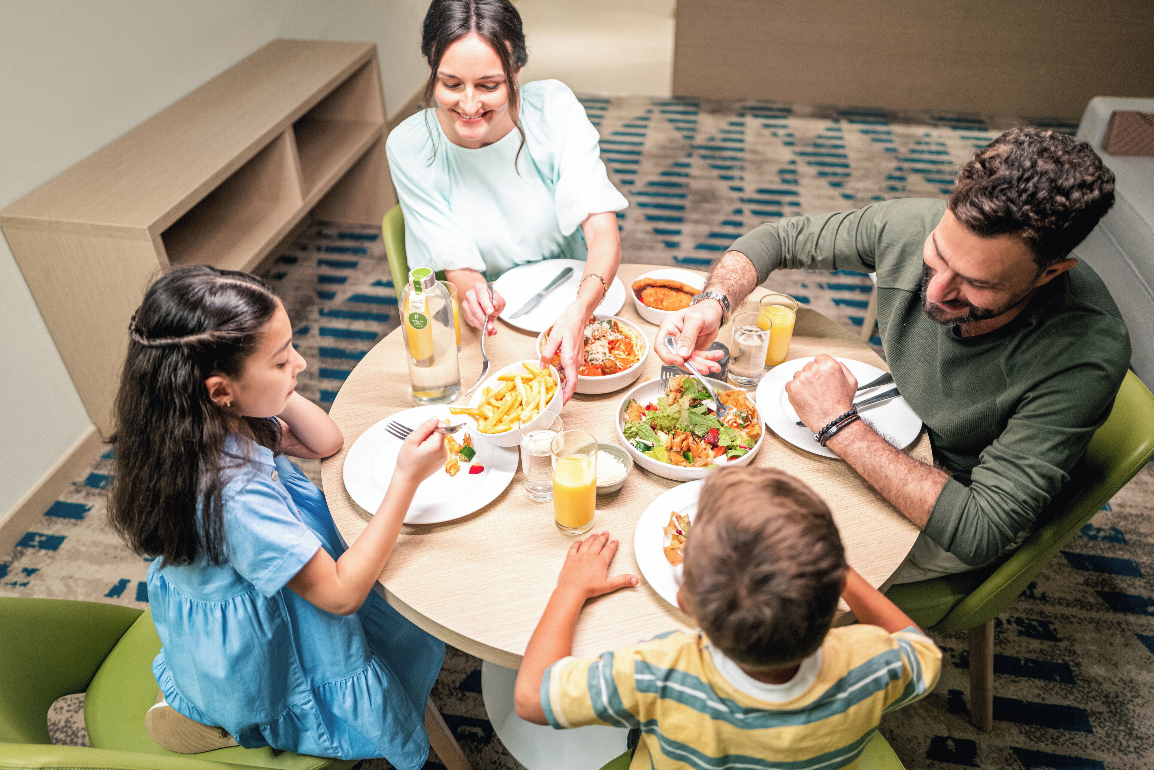 A family dining at a round table with various dishes, drinks, and a bottle of water.