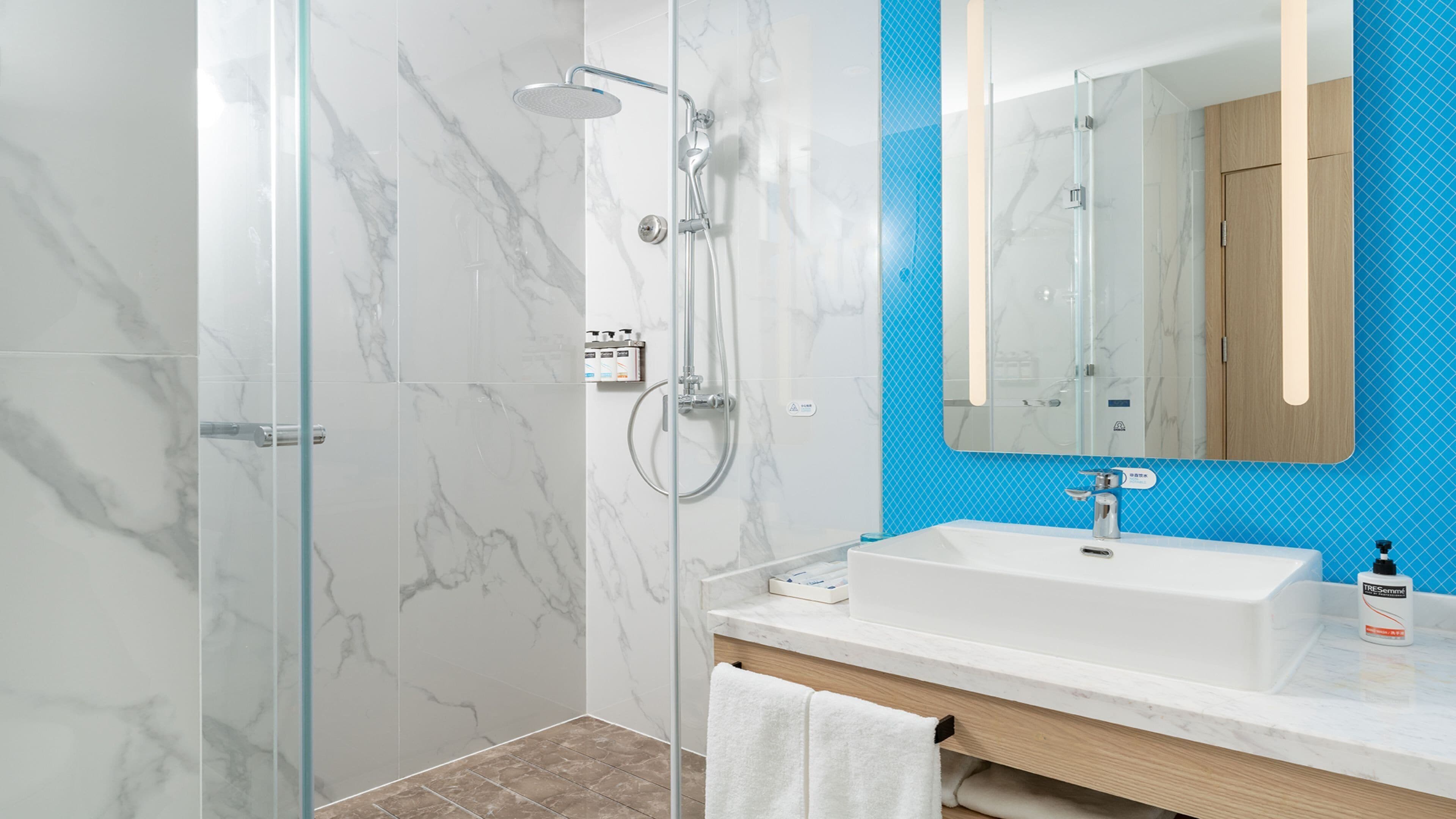 A modern bathroom with a glass shower enclosure, a white sink, and a mirror with a blue accent wall.