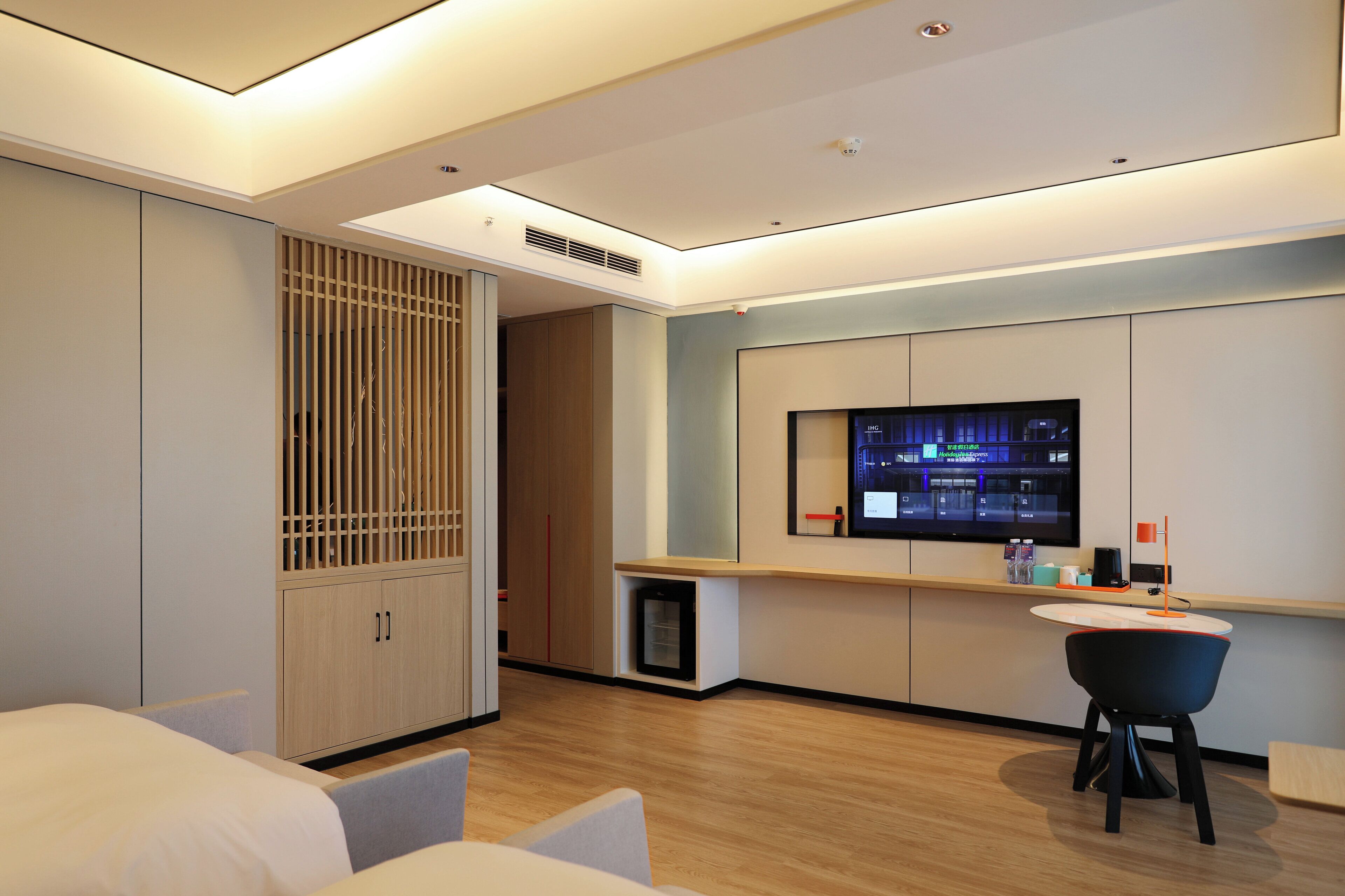 A modern hotel room with a large bed, a desk with a computer, and a TV mounted on the wall.
