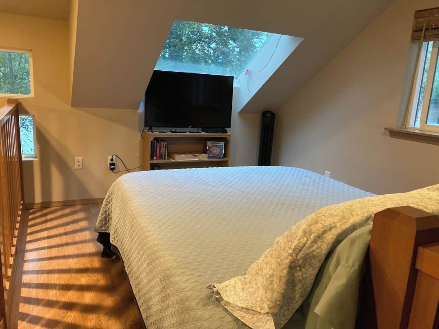 A bedroom with a large bed, a television on a stand, a bookshelf, and a skylight.