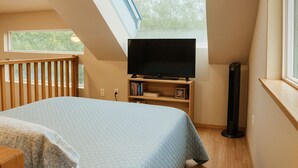 A bedroom with a bed, a TV on a stand, a bookshelf, and a standing heater.