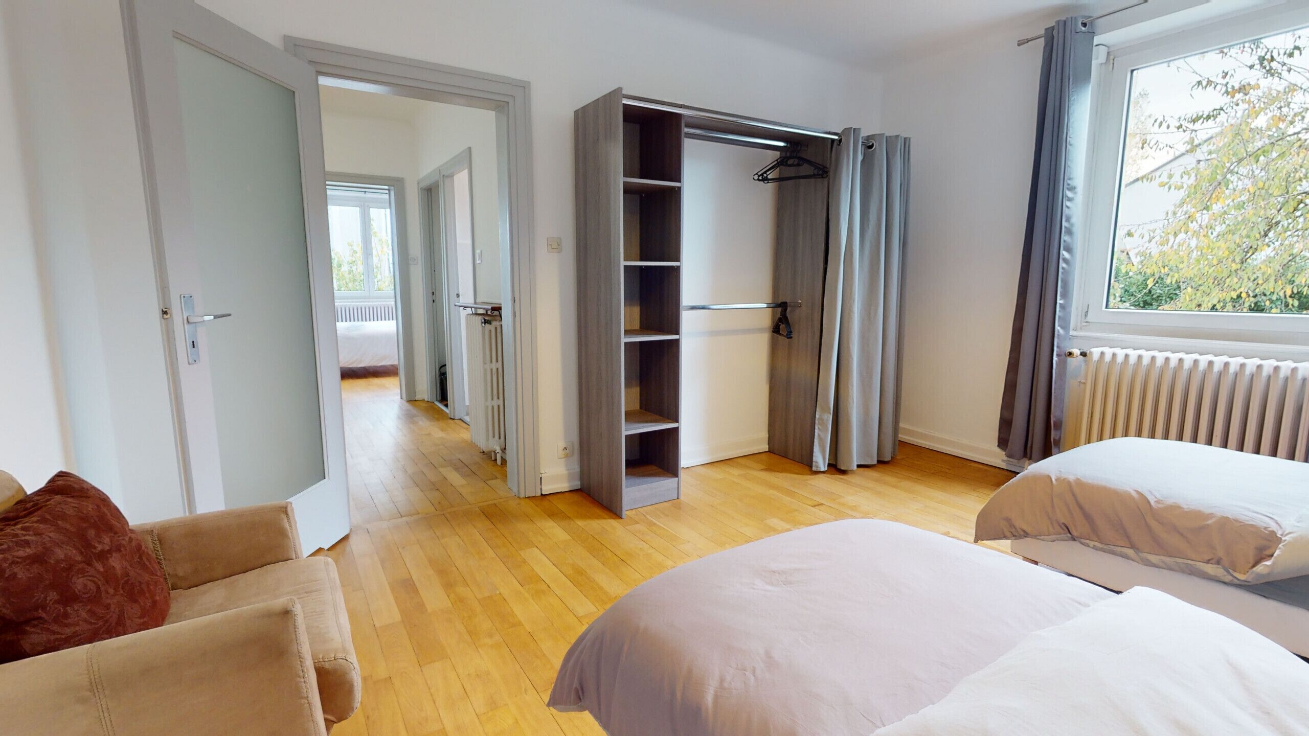 A bedroom with a wooden floor, a bed, a wardrobe, and a window with curtains.