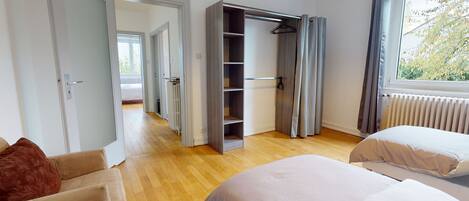A bedroom with a wooden floor, a bed, a wardrobe, and a window with curtains.