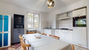 Eine moderne Küche mit weißen Schränken, einem Esstisch mit Stühlen, einem Einbauofen und einem Fenster, das natürliches Licht hereinlässt.