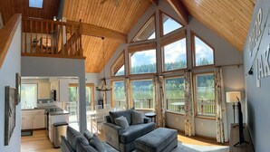 A spacious living area with a high ceiling, large windows offering a view of a lake, and a cozy seating area with a fireplace. - ~Lakefront Property ~ 23 miles to Mt. Rainier! (Eatonville)
