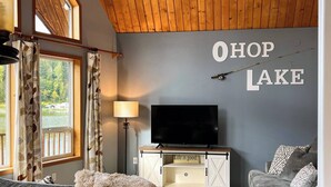 A cozy living room with a large TV, a wooden ceiling, and a wall sign that reads "OHOP LAKE". - ~Lakefront Property ~ 23 miles to Mt. Rainier! (Eatonville)